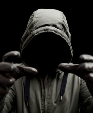 A terrifying mysterious man wearing a hooded jacket with arms raised in a strangling or attacking pose. Shot against a black background.